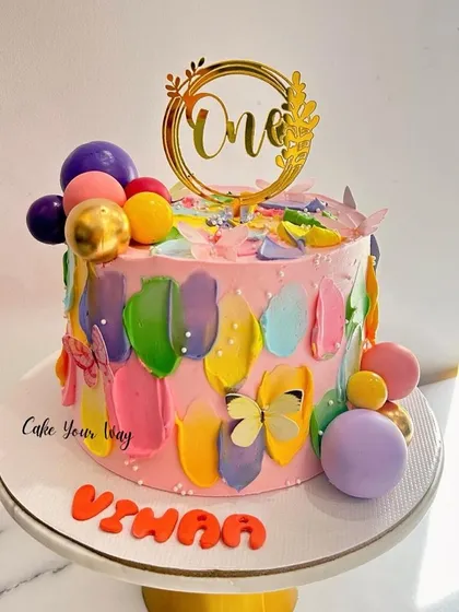 Sweet hues and tasty views on this colorful first birthday cake, decorated with abstract buttercream strokes and butterflies.