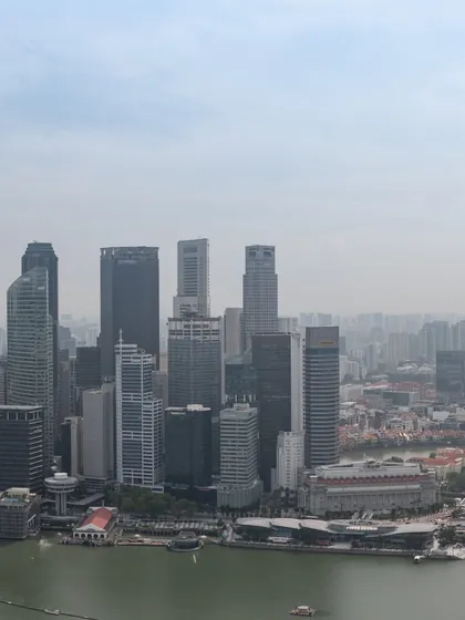 A daytime photograph of the Singapore skyline, showing the dense cluster of skyscrapers in the central business district.