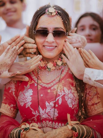 A fun and quirky Haldi moment where the bride sports sunglasses while being surrounded by the hands of her family, ready to apply turmeric.