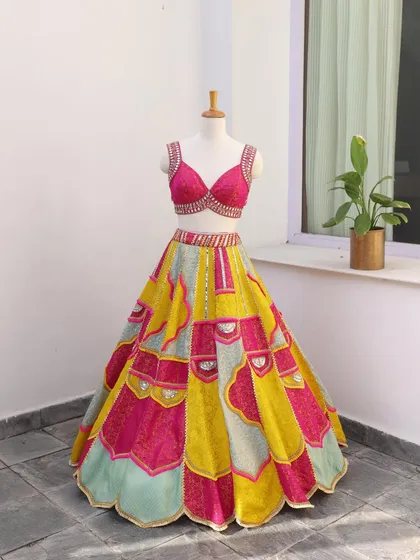 Isn't this just perfect for your Mehendi or Haldi? This multi-colored lehenga with a hot pink blouse and mirror work is designed to be playful and eye-catching.