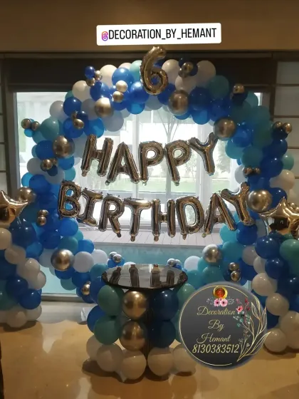 A classic circular balloon arch for a 6th birthday. The blue, white, and silver chrome balloons create a festive frame around the cake-cutting table, with "Happy Birthday" foil letters in the center.