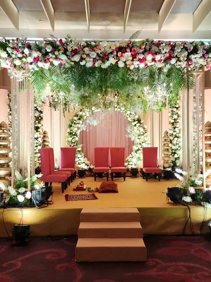 This mandap design features a circular floral arch at the center, with pillars covered in white flowers and a canopy of fresh greenery, perfect for a modern yet romantic ceremony.
