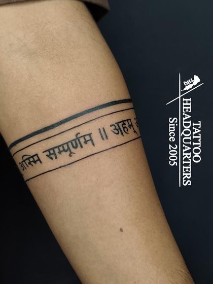 An armband tattoo featuring a Sanskrit shloka, "Asmi Sampurnam," meaning "I am complete."