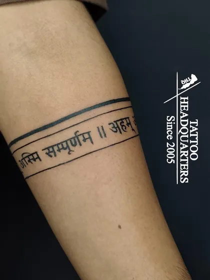 An armband tattoo featuring a Sanskrit shloka, "Asmi Sampurnam," meaning "I am complete."