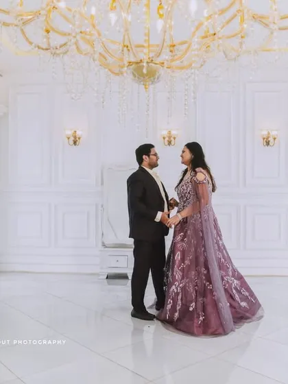 An elegant couple's portrait in a grand, all-white studio with a crystal chandelier. This showcases the sophisticated and royal vibe we can create for your indoor shoot.