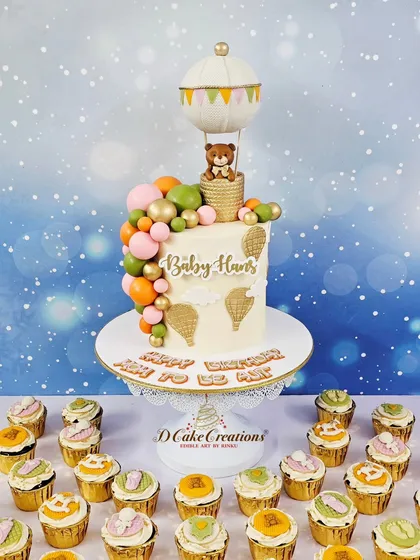 A beautiful hot air balloon themed cake designed for singer Ajit Kaur's baby shower and birthday. The design features a hand-sculpted teddy bear, a cascade of pastel and gold spheres, and delicate hot air balloon details, all surrounded by matching custom cupcakes. This is how we create elegant and cohesive dessert tables for baby showers.