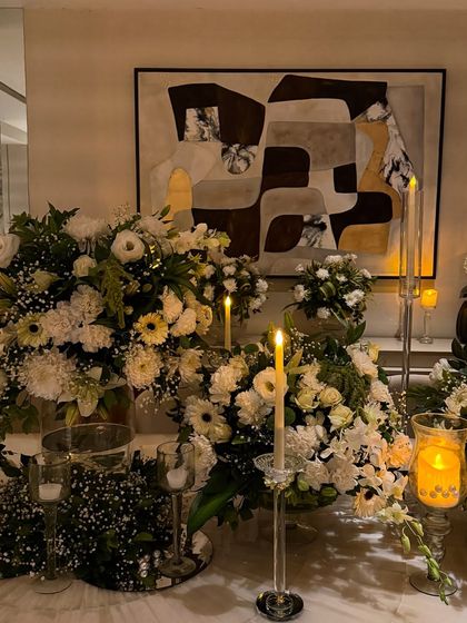 A beautiful tablescape featuring lush arrangements of white flowers and greenery, illuminated by the warm glow of numerous candles. This setup is perfect for an elegant dinner party or reception.