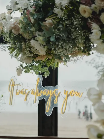 The all-important detail. A custom neon sign saying 'It was always you' adds a deeply personal and modern touch to this romantic seaside proposal decor.