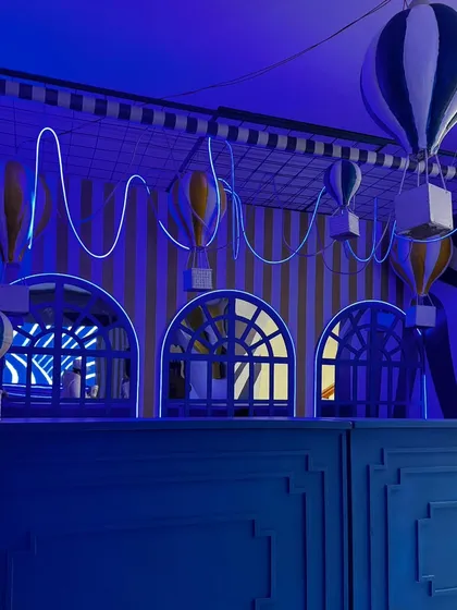 An evening shot of the indoor bar area, where miniature hot air balloons and neon lights create a whimsical and enchanting atmosphere. The design continues the blue and white theme.