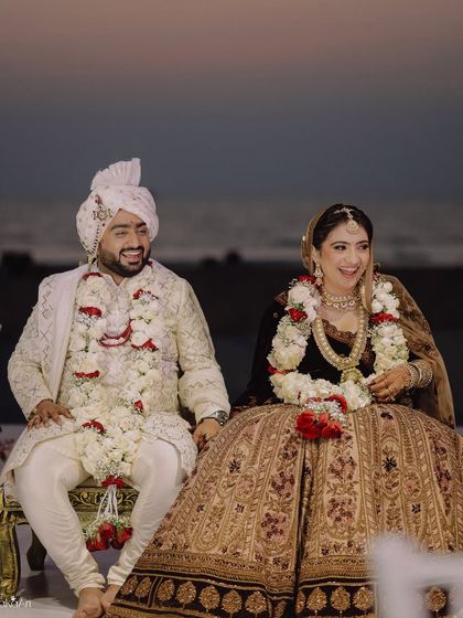 The couple shares a laugh while seated at the mandap, a candid moment of joy amidst the formal rituals.
