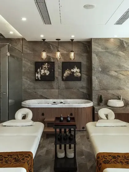 This spa room is designed for ultimate relaxation. The space combines earthy decor, like the stone accent wall and wooden elements, with modern amenities like a jacuzzi tub. Soothing, neutral colors and soft lighting complete this tranquil retreat.