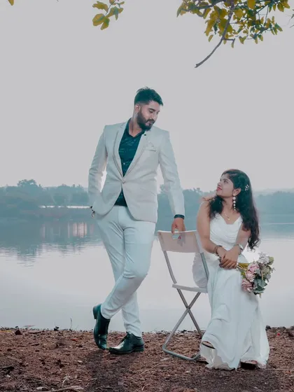 A classic romantic scene by the water. The bride is seated with a bouquet while the groom stands beside her, creating a timeless and elegant image.