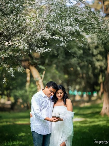 A couple sharing a sweet moment under a canopy of white blossoms. This image captures the romance and tenderness of awaiting a new life together.