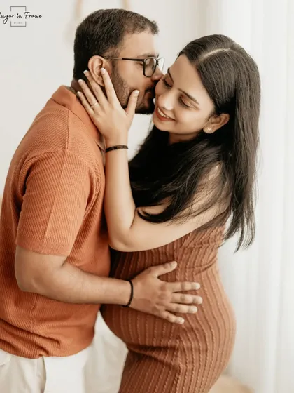 A sweet and affectionate moment during a maternity session. The husband-to-be gives his wife a gentle kiss on the cheek, showcasing their close bond.