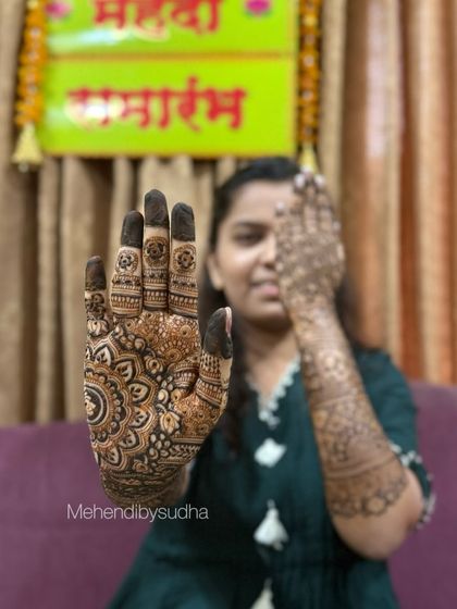 A happy bride-to-be, Shreya, showing off her engagement mehendi with a beautiful mandala design on her palm.