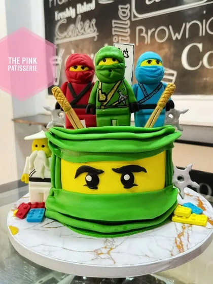 A powerful Lego Ninjago cake featuring the Green Ninja's mask and three character figures on top. The details make this a standout cake for any fan of the series.