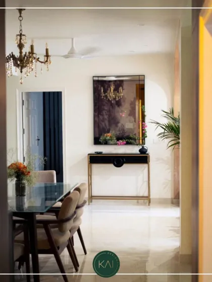 This view into a dining area showcases a sleek glass-topped table with brass-finished legs, paired with comfortable upholstered chairs. The scene is completed by a matching console table, creating a harmonious and elegant space.