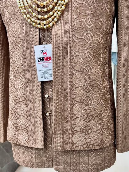 A close-up of the Mocha Brown Jodhpuri suit, accessorized with a multi-layered pearl necklace. The intricate texture of the fabric is clearly visible.