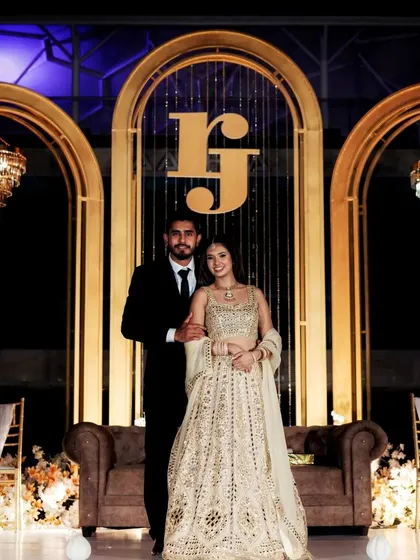 A sophisticated reception stage design. I created a custom monogram 'RJ' set against a backdrop of golden arches and crystal strings, flanked by two beautiful chandeliers for a royal touch.
