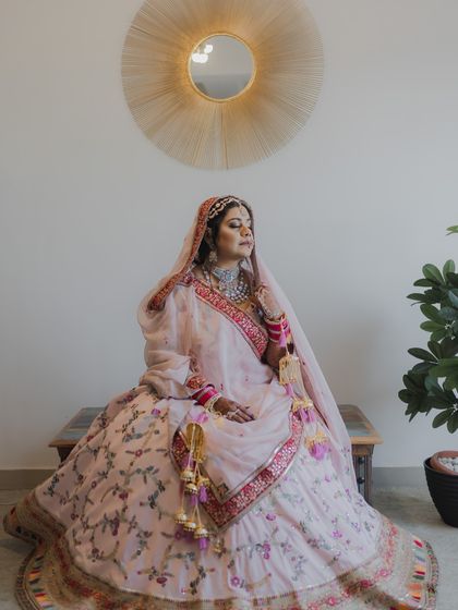 A full-length portrait of the bride seated, showcasing her magnificent floral lehenga and regal posture.