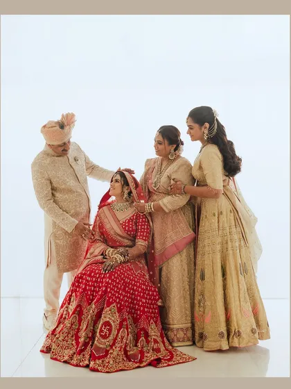 A beautiful and emotional family portrait. The bride is seated in her stunning red lehenga, surrounded by the love and support of her parents and sister.