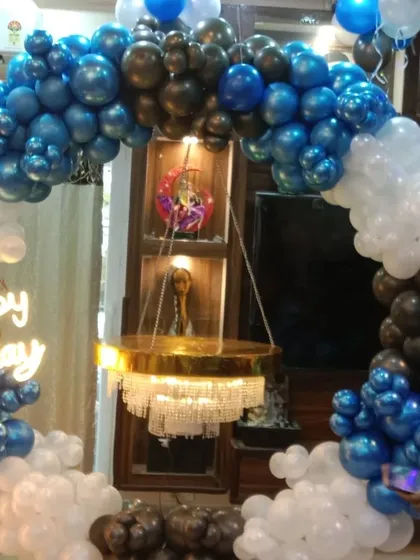 A striking balloon arch in shades of metallic blue, black, and white clouds. This design frames a home's display unit, incorporating a hanging chandelier-style cake stand.