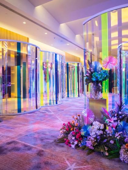 The full view of the iridescent tunnel entrance, lined with stunning, colorful floral arrangements. The design guides guests through a journey of color and light before they even reach the main event space.