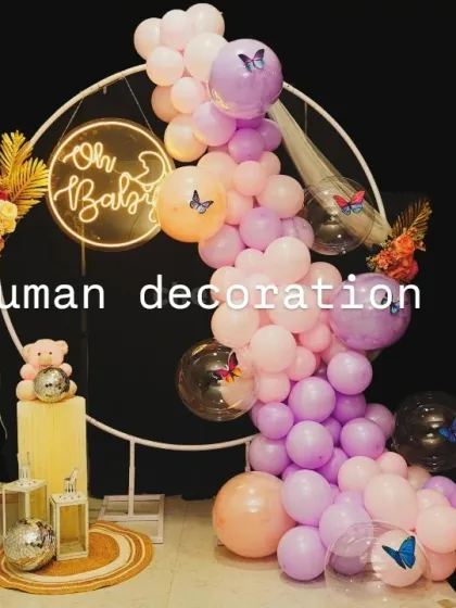 A chic 'Oh Baby' setup for a baby shower. The decor includes a balloon garland in pastel pink and purple on a ring frame, with butterfly and teddy bear props.