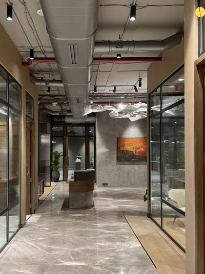 The central spine of 'Project LH' in South Bombay. Glass-walled cabins line the corridor, ensuring that natural light penetrates deep into the office. The design balances the need for private offices with a feeling of openness and connection.
