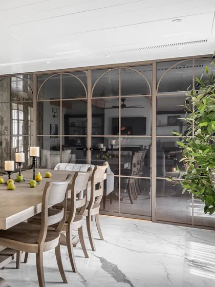 A beautiful arched glass partition separates the dining room from the adjacent music room, allowing for visual connection while maintaining acoustic privacy. The design adds an elegant architectural element.