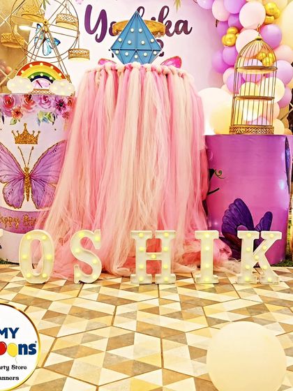 A close-up of a butterfly-themed dessert table, showing the 'YOSHIKA' marquee letters and a tulle-draped plinth.