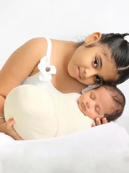 A sweet, angelic pose with an older sister gently holding her swaddled newborn sibling amidst soft, cloud-like props. This setup creates a dreamy and serene atmosphere.