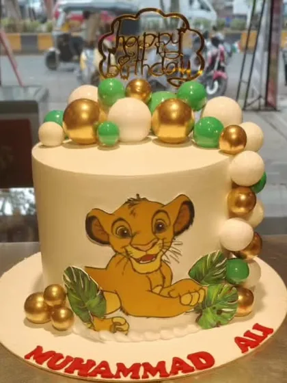 A charming Simba cake perfect for a Lion King themed party. This design features a cute Simba illustration, surrounded by a border of green, white, and gold spheres for a modern touch.