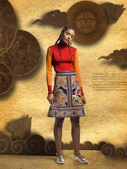 This image showcases a designer skirt with detailed traditional patterns. The styling with a simple, color-blocked top allows the skirt to be the hero piece in this full-length catalogue shot.