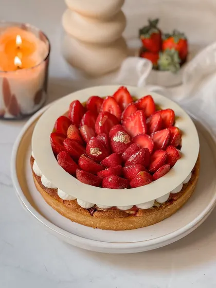 A full view of our elegant Strawberry Tart, with its distinctive white chocolate ring framing a mound of sliced strawberries. Edible gold leaf adds a final touch of luxury to this seasonal patisserie item.