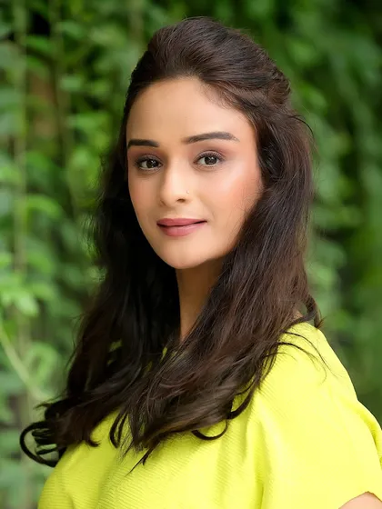 A natural outdoor headshot of Harleen Kaur. The soft, diffused light from the foliage creates a beautiful, gentle look.