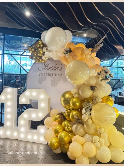 A side view of the golden-hued balloon arch, showing the mix of different balloon sizes and textures that create a rich, luxurious feel.