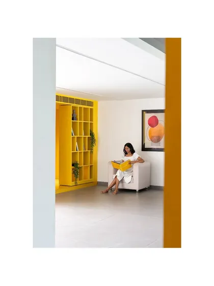 A quiet reading nook within 'The Amber Encase' clubhouse. The vibrant yellow shelving unit acts as both storage and a sculptural element, framing a cozy space for relaxation.