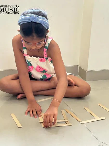 True learning is hands-on. Here, a student is deeply focused on creating rhythmic patterns using popsicle sticks. This tactile approach helps demystify music notation, making it an accessible and engaging activity for children.