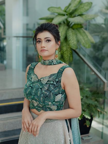 A modern and chic look for a cocktail party or Mehendi. The client is wearing a unique green lehenga with a leaf-patterned blouse, paired with a sleek top knot.