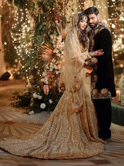Another angle of this glamorous couple, showcasing the bride's magnificent train and the intricate gold embroidery on the groom's outfit.