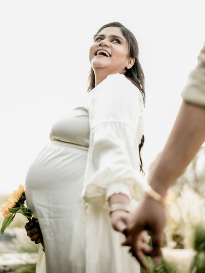 A joyful "follow me" shot, with the mom-to-be in a flowing white dress, laughing as she leads her partner.