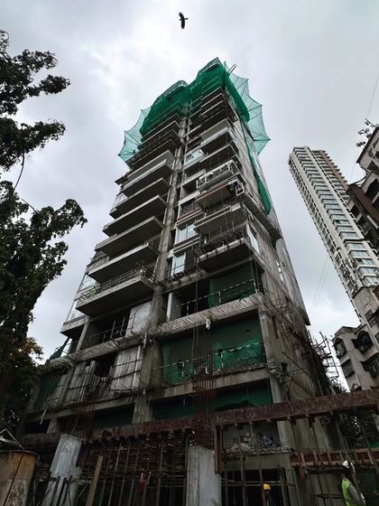 A residential tower under construction, viewed from below. The green safety netting and exposed concrete give a sense of the ongoing work, as the building steadily rises to join the city skyline.