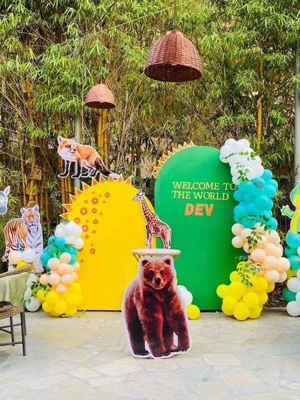 A 'Welcome to the World of Dev' party with a woodland animals theme. The outdoor setup features bright green and yellow backdrops with various animal cutouts.