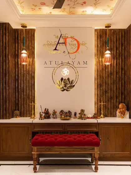 This pooja room features dark wood fluted panels, a tufted red bench for seating, and a floral wallpapered ceiling for a touch of divine elegance.