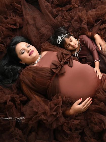 A tender moment of rest. The mother and daughter lie together, nestled in the soft brown fabric of the gown, a beautiful image of their close bond.