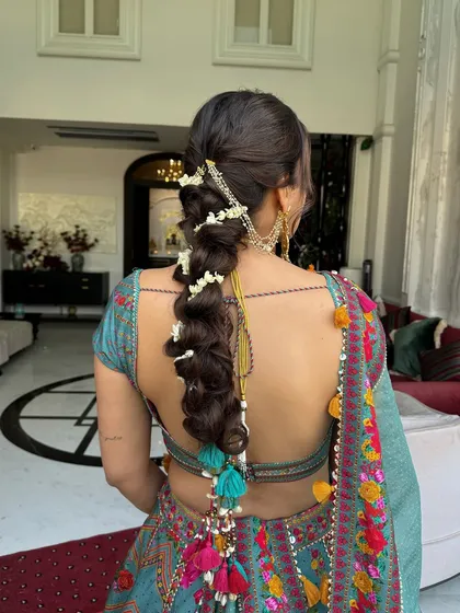 A playful yet traditional bubble braid for a Mehendi ceremony, woven with fresh mogra flowers and finished with vibrant tassels. This look is perfect for the bride who wants a fun, bohemian hairstyle that is still deeply rooted in Indian tradition.