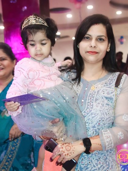 A mother holds her daughter, who is dressed like a little princess with a tiara.