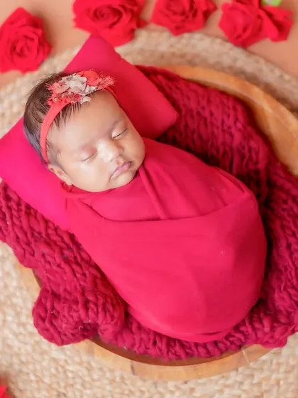 Surrounded by red roses, this sleeping baby looks like a precious gift.