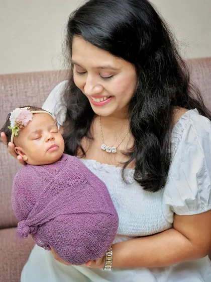 A mother's gentle smile as she holds her sleeping newborn. The soft lighting and simple background keep the focus on this beautiful, quiet moment.